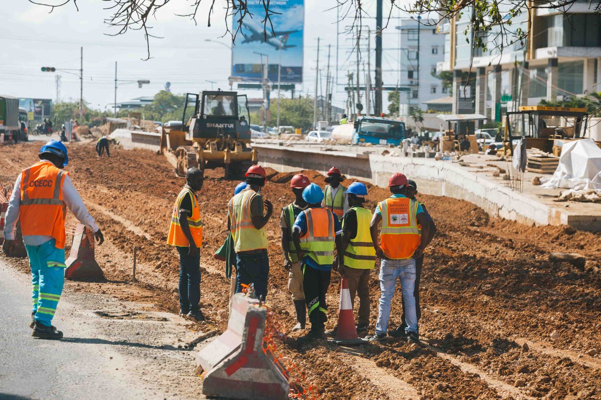 A road-construction crew in hi-vis vests working on an outdoor infrastructure site.